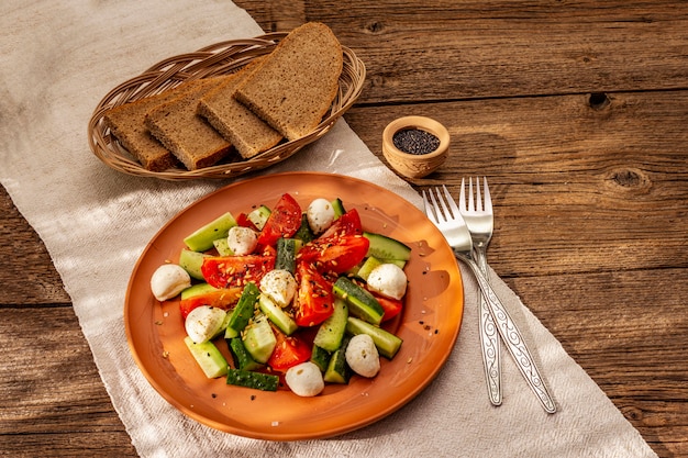 Ensalada fresca de tomate, pepino y mozzarella bebé. Almuerzo soleado con pan crujiente.