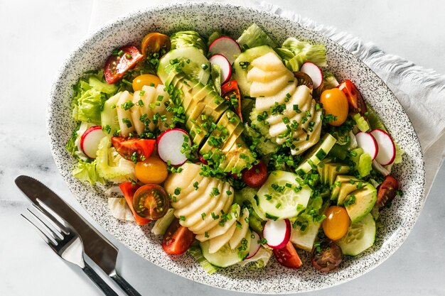 Ensalada fresca de verano de frutas y verduras en un plato ovalado sobre una mesa con cubiertos. comida sana