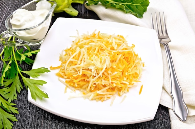 Ensalada fresca de zanahorias y repollo colinabo en un plato de crema agria en una servilleta de salsera y tenedor sobre un fondo de madera