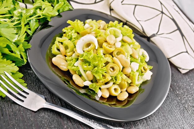 Ensalada de frijoles, aceitunas, tallos de apio, cebolla y lechuga, aderezado con aceite vegetal en un plato, remolque