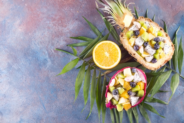 La ensalada de fruta exótica sirvió por la mitad una fruta del dragón y piña con la hoja de palma en el fondo de piedra, espacio de la copia. Vista superior