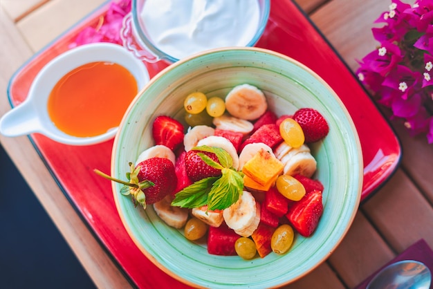 Ensalada de fruta fresca y saludable en la mesa del desayuno. Ensalada de frutas en tazón con miel y yogur griego.