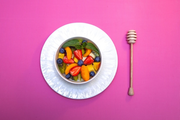 Ensalada de frutas con cuchara de miel de madera sobre fondo rosa