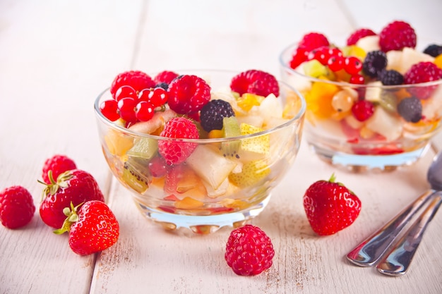 Ensalada con frutas frescas y bayas en tazones sobre el fondo blanco