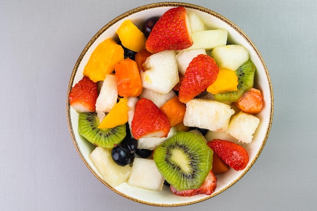 Ensalada de frutas frescas en un bol Frutas multicolores y tropicales Piña mango uva fresa papaya melón kiwi Adicional con castañas y granola Vista superior Enfoque selectivo