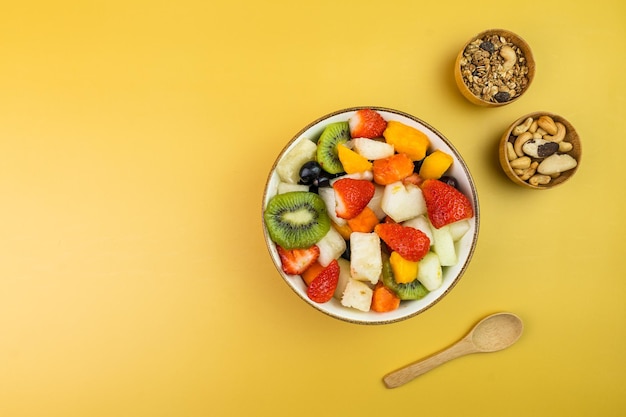 Ensalada de frutas frescas en un bol Frutas multicolores y tropicales Piña mango uva fresa papaya melón kiwi Adicional con castañas y granola Vista superior Enfoque selectivo