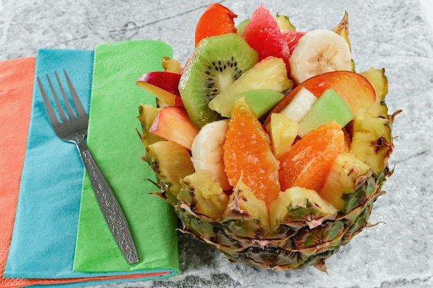 Ensalada de frutas frescas con kiwi, plátano, melocotón, naranja, rojo, naranja, albaricoque y melón en un tazón de piña