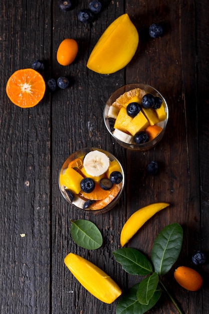 Ensalada de frutas frescas con varios tipos de bayas y cítricos, mango servido en un recipiente de vidrio, colocado sobre una mesa de madera