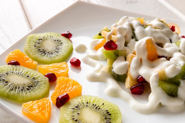 Ensalada de frutas con helado plato blanco junto a la fruta en rodajas