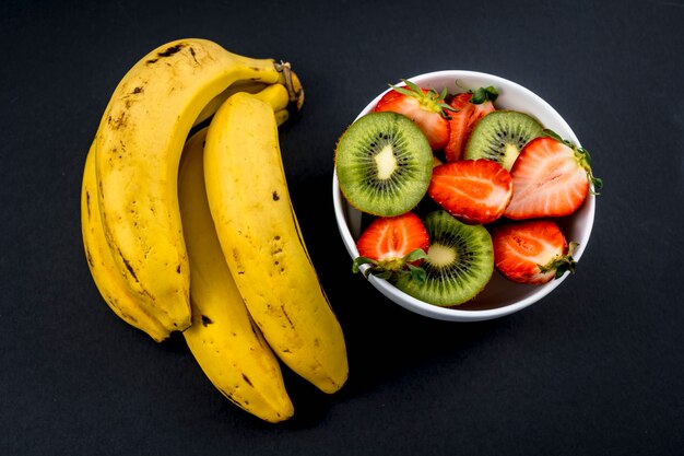 Una ensalada de frutas junto a un racimo de plátanos en negro