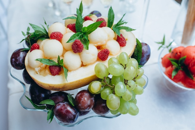 Ensalada de frutas de melón, frambuesa, menta, uvas en un plato de helado de vidrio, de cerca.