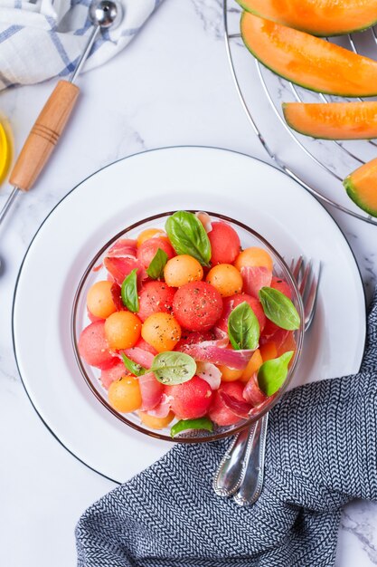 Ensalada de frutas con melón melón, sandía y jamón serrano en un recipiente en la mesa de la cocina