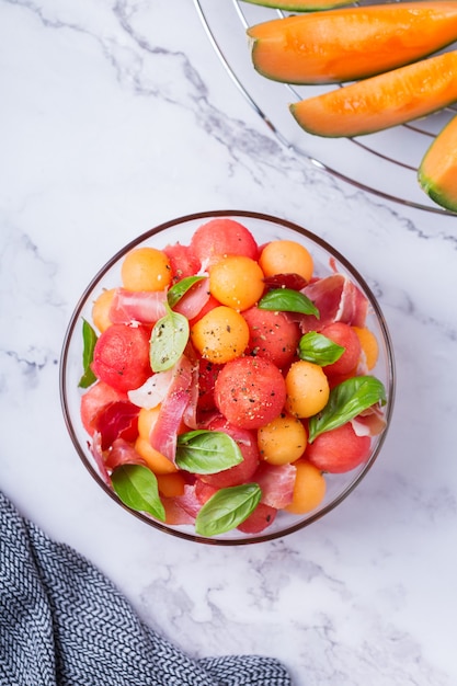 Ensalada de frutas con melón melón, sandía y jamón serrano en un recipiente en la mesa de la cocina