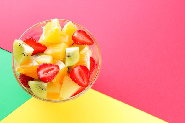 Ensalada de frutas de piña, kiwi, naranja y fresa Frutas en rodajas multicolores en un recipiente transparente sobre fondo multicolor Copiar espacio