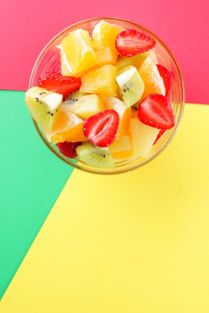 Ensalada de frutas de piña, kiwi, naranja y fresa Frutas en rodajas multicolores en un recipiente transparente sobre fondo multicolor Copiar espacio