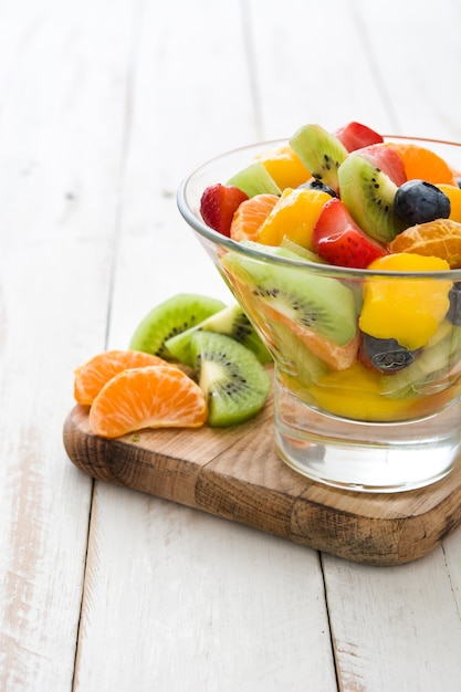 Ensalada de frutas en un recipiente de cristal en la mesa de madera blanca.