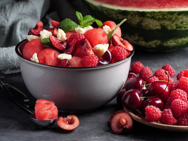 Ensalada de frutas con sandía, queso feta, menta, frambuesas y cerezas sobre un fondo gris