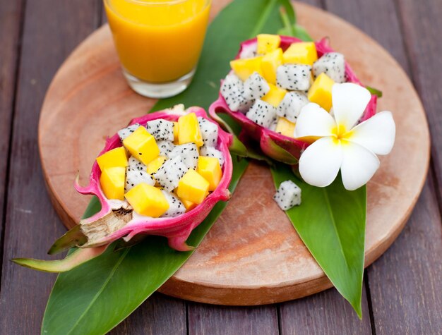 Foto ensalada de frutas tropicales en cuencos de frutas de dragón pitahaya con un vaso de jugo de mango y una flor sobre un fondo de madera