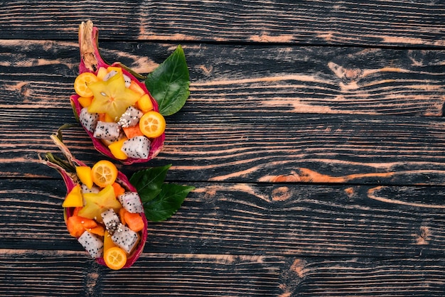 Ensalada de Frutas Tropicales Servida en media Fruta del Dragón. Papaya, rambután, tamarindo, fruta de cactus, mango. Sobre un fondo de madera. Vista superior.