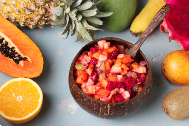 Ensalada de frutas tropicales en un tazón de coco sobre un fondo azul claro, primer plano, formato horizontal