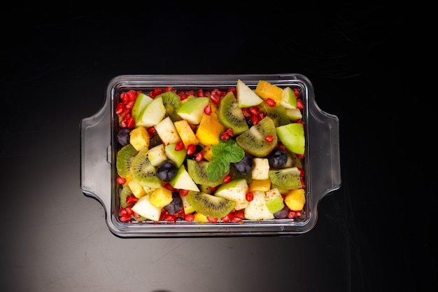 Ensalada de frutas variadas dispuesta en una vajilla rectangular transparente y adornada con hoja de menta.