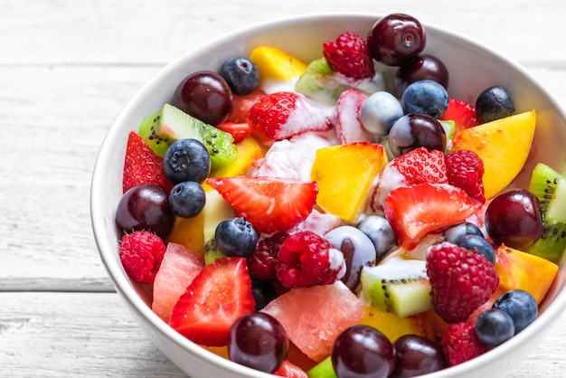 Ensalada de frutas con yogur, sandía, fresa, cereza, arándano, kiwi, frambuesa y duraznos en un tazón. comida sana