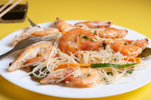 Ensalada funchosa de primer plano con gambas en un plato blanco sobre un fondo amarillo