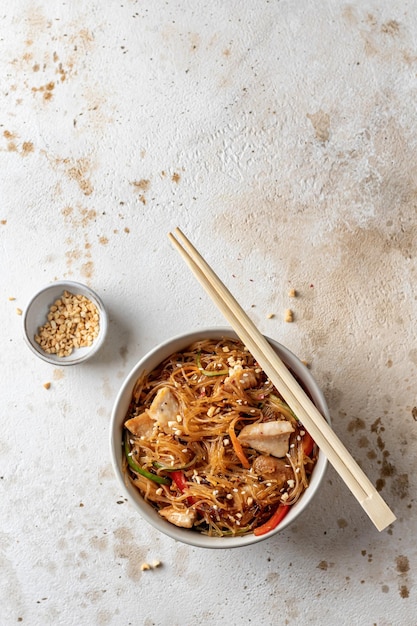 Ensalada Funchose con pollo y verduras en un tazón con palillos de madera sobre fondo marrón texturizado con espacio para copiar Menú de comida Vista superior