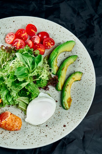 Ensalada gourmet con salmón asado, salsa de crema, aguacate, espinacas, lechuga, mozzarella y tomates cherry en negro. Deliciosa ensalada de mariscos. De cerca