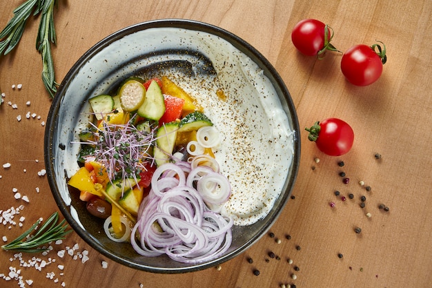 Ensalada griega clásica con tomate, cebolla, pepino, queso feta y aceitunas negras con aceite de oliva en un plato blanco sobre una superficie de madera