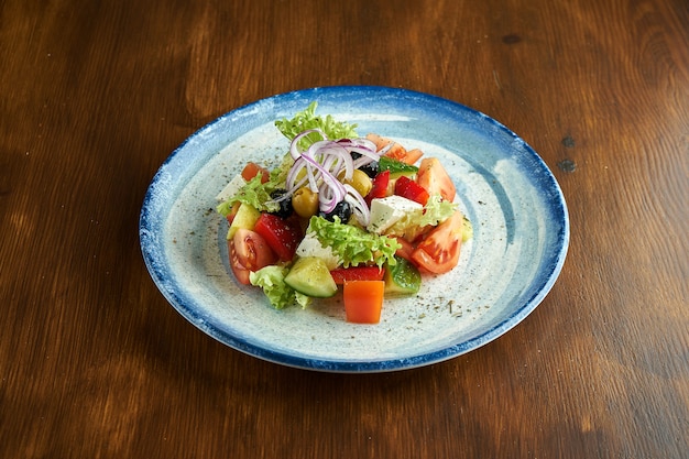 Ensalada griega clásica con tomates, pepinos, cebollas rojas, queso feta y aceitunas, servida en un plato azul sobre una superficie de madera