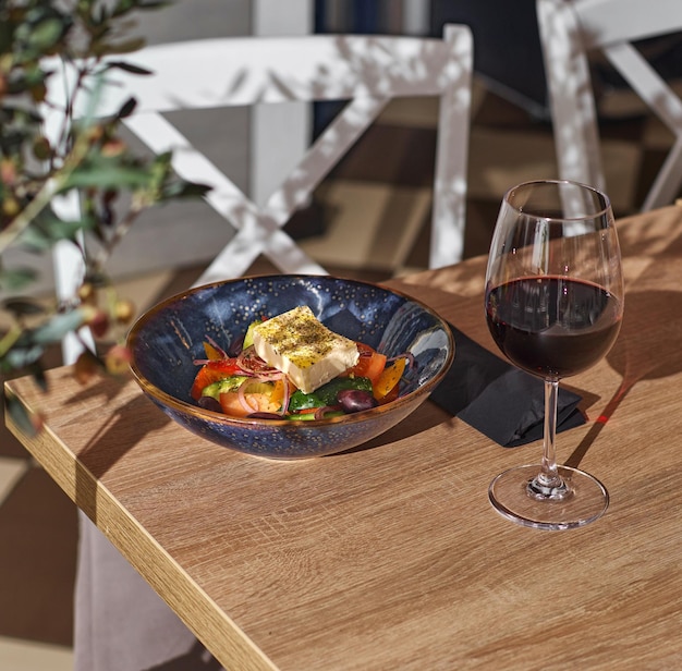 Ensalada griega clásica de tomates, pepinos y queso Plato de ensalada y una copa de vino en una mesa en un restaurante