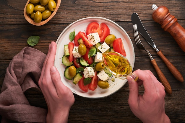 Ensalada griega Ensalada griega fresca con verduras frescas tomate pepino aceitunas verdes queso feta y manos de hombre sobre fondo de mesa de madera oscura vieja Vista superior