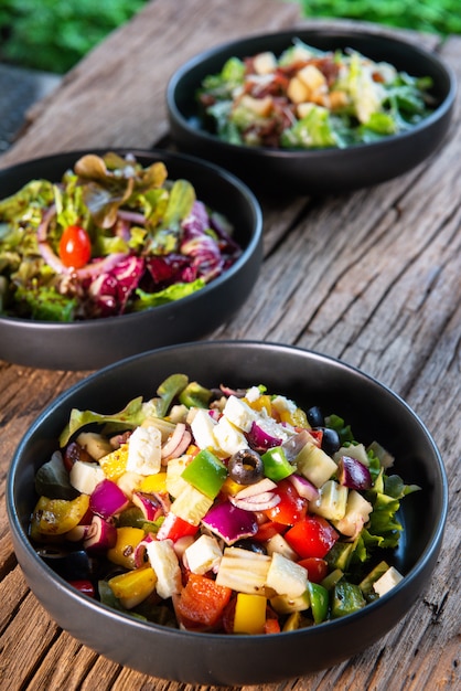 Ensalada griega, ensalada japonesa, ensalada César, en un tazón de cerámica negra, sobre una mesa de madera, para amantes de la salud, amantes de las verduras.