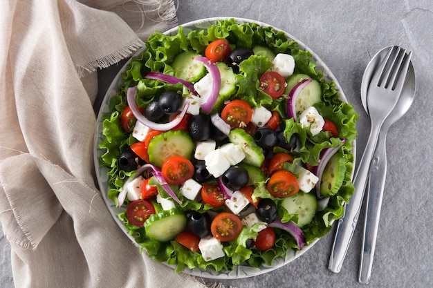 Ensalada griega fresca en placa con aceituna negra, tomate, queso feta, pepino y cebolla sobre fondo gris vista superior