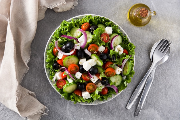 Ensalada griega fresca en placa con aceituna negra, tomate, queso feta, pepino y cebolla sobre fondo gris vista superior