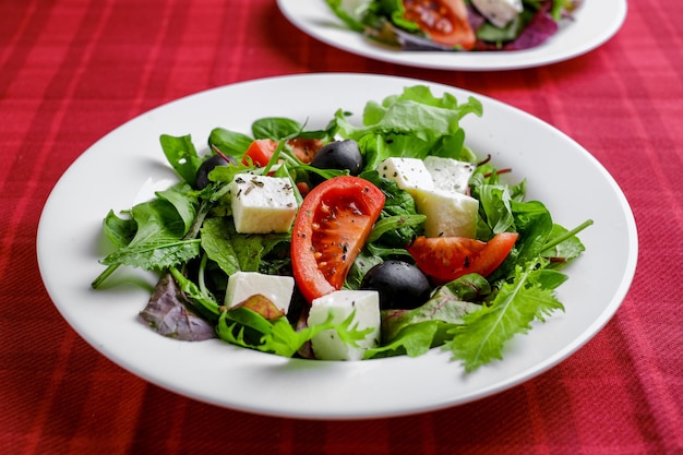 Foto ensalada griega fresca en plato blanco sobre fondo rojo. primer plano y vista superior.