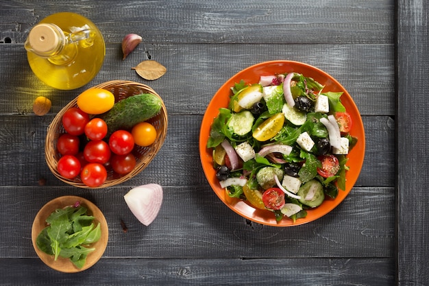 Ensalada griega fresca en plato e ingredientes sobre mesa de madera