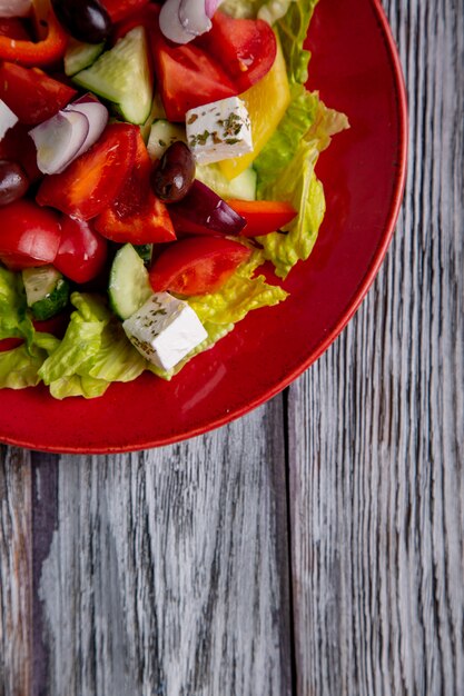 Ensalada griega de pepino fresco, tomate, pimiento dulce, lechuga, cebolla roja, queso feta y aceitunas con aceite de oliva en madera. Comida sana