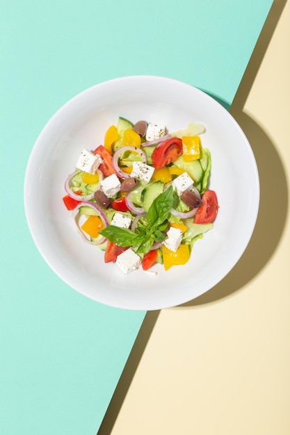 Ensalada griega en plato blanco sombras duras sobre azul y amarillo foto de alta calidad