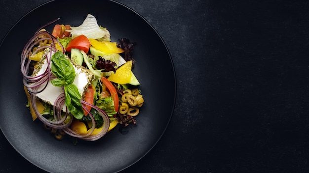 Foto ensalada griega en un plato oscuro sobre un fondo oscuro