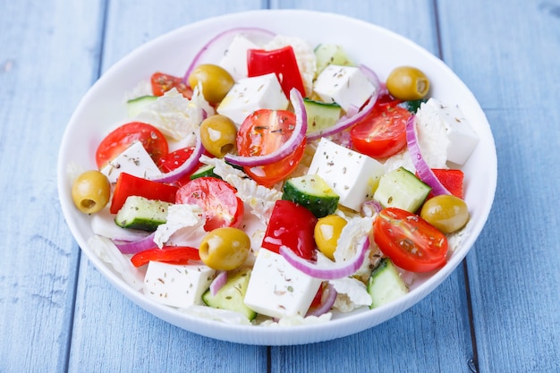 Ensalada griega. Plato tradicional griego. Comida vegetariana saludable. Verduras frescas y queso feta en un plato blanco. Primer plano, fondo azul.