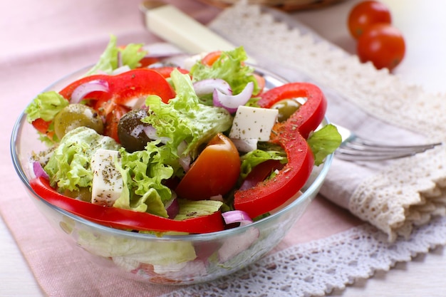 Foto ensalada griega en plato de vidrio con tenedor en servilleta y fondo de mesa de madera