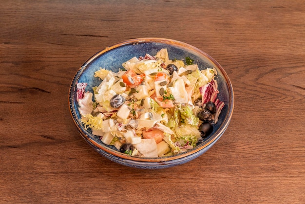 Ensalada griega con semillas de yogur, aceitunas negras, lechuga y tomate picado en un bol azul