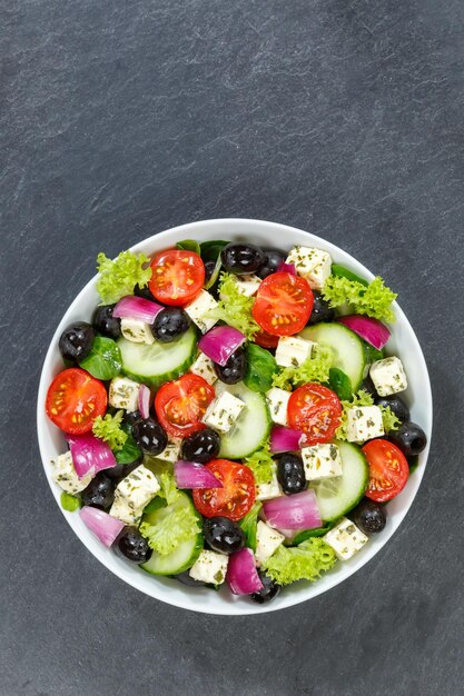 Ensalada griega con tomates frescos, aceitunas y queso feta, alimentos saludables para comer desde arriba, formato vertical con espacio de copia en una pizarra