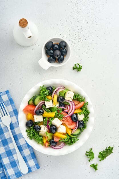 Ensalada griega tradicional de pepino fresco, tomate, pimiento, lechuga, cebolla roja, queso feta y aceitunas con aceite de oliva en un plato blanco. Comida sana, vista superior.