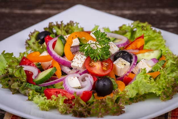 Ensalada griega de verduras frescas en un plato blanco sobre la mesa de madera, cerrar