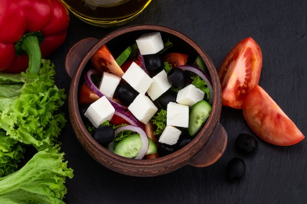 Ensalada griega con verduras frescas, queso feta y aceitunas negras sobre un fondo oscuro. Vista superior. .