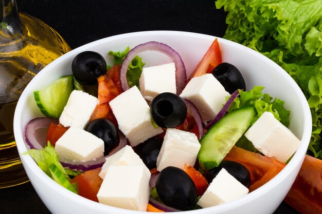 Ensalada griega con verduras frescas, queso feta y aceitunas negras sobre un fondo oscuro.