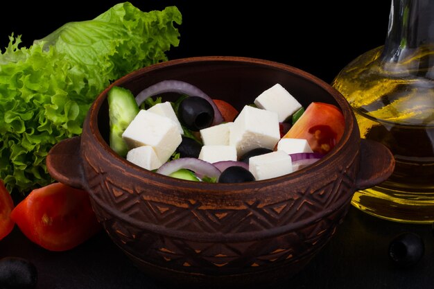 Ensalada griega con verduras frescas, queso feta y aceitunas negras sobre un fondo oscuro.